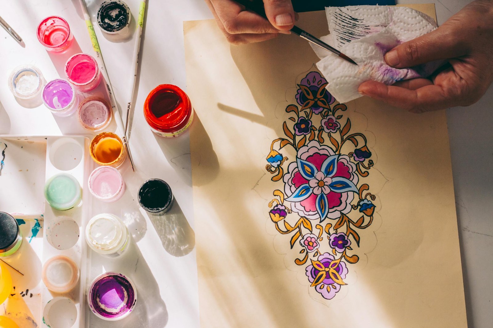 Artist meticulously creates colorful painting using vibrant paints and brushes on a desk.